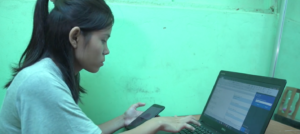 Photograph of a female freelance translator working on a laptop with a phone in her hand