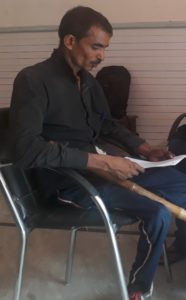 Rajan (name changed) reads a document while his make-shift bamboo walking stick rests on the chair he is seated on